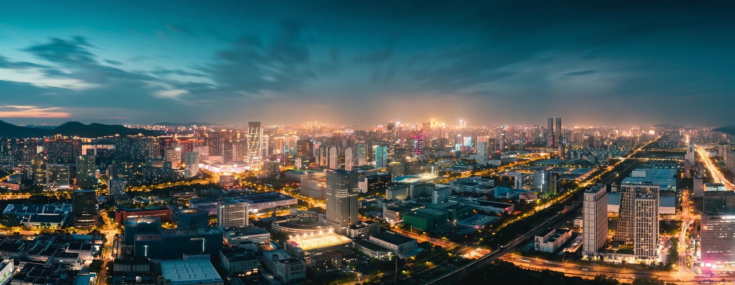 A panoramic night view of a city glowing beneath a blue hour sky