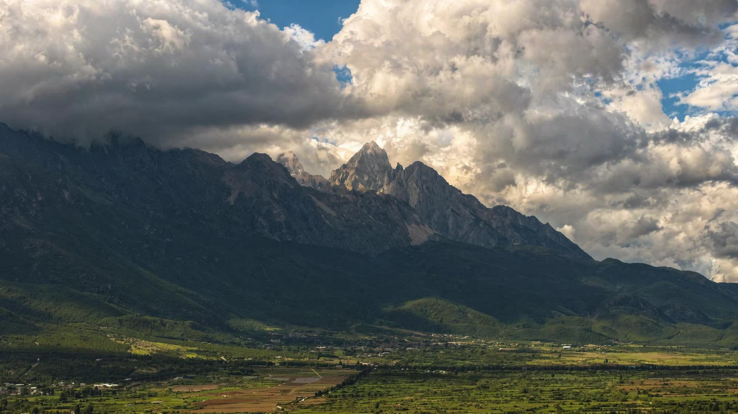 A sharp mountain ridge catches light beneath towering storm clouds