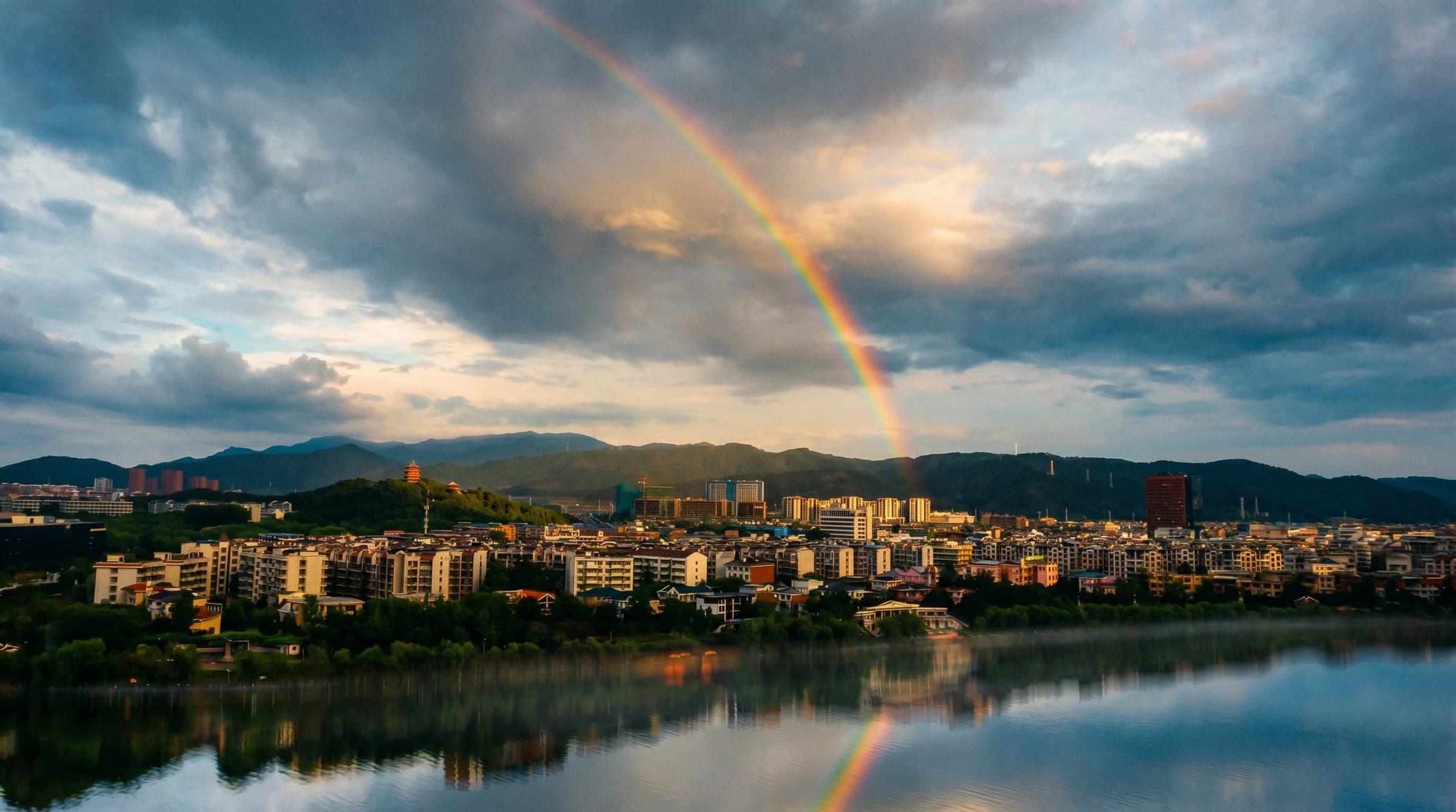 A rainbow arcs over a lakeside city and its mountain skyline