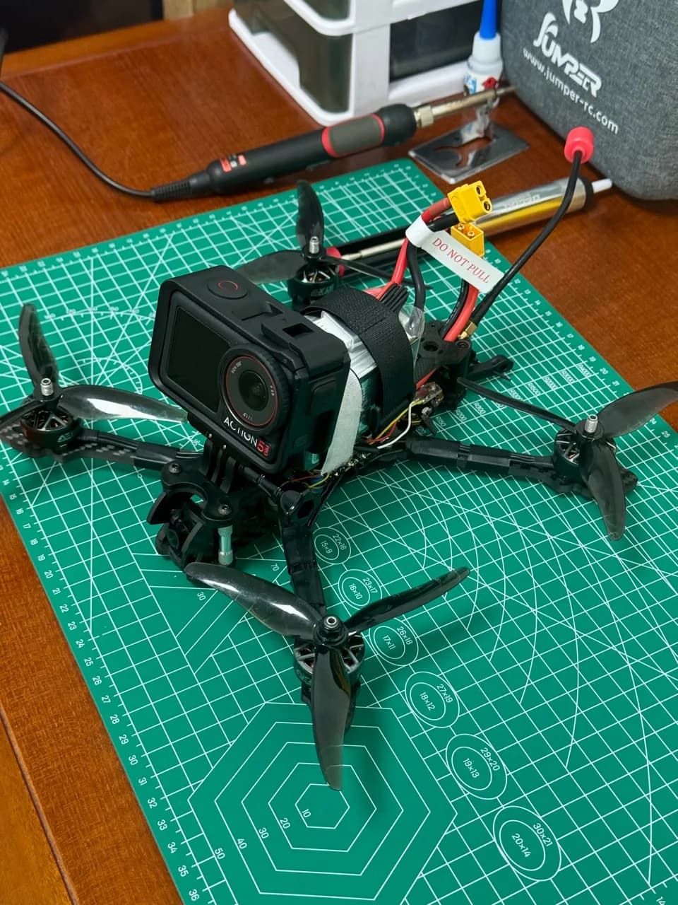 FPV drone fitted with an action camera and battery on a green cutting mat